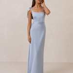 Woman wearing a light blue gown with tie straps on a beige background