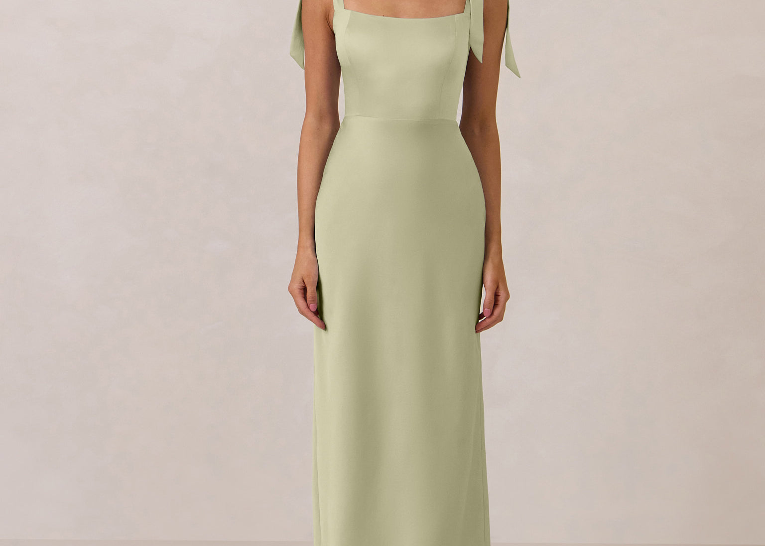 Woman wearing a pistachio gown with tie straps on a plain background