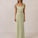 Woman wearing a pistachio gown with tie straps on a plain background