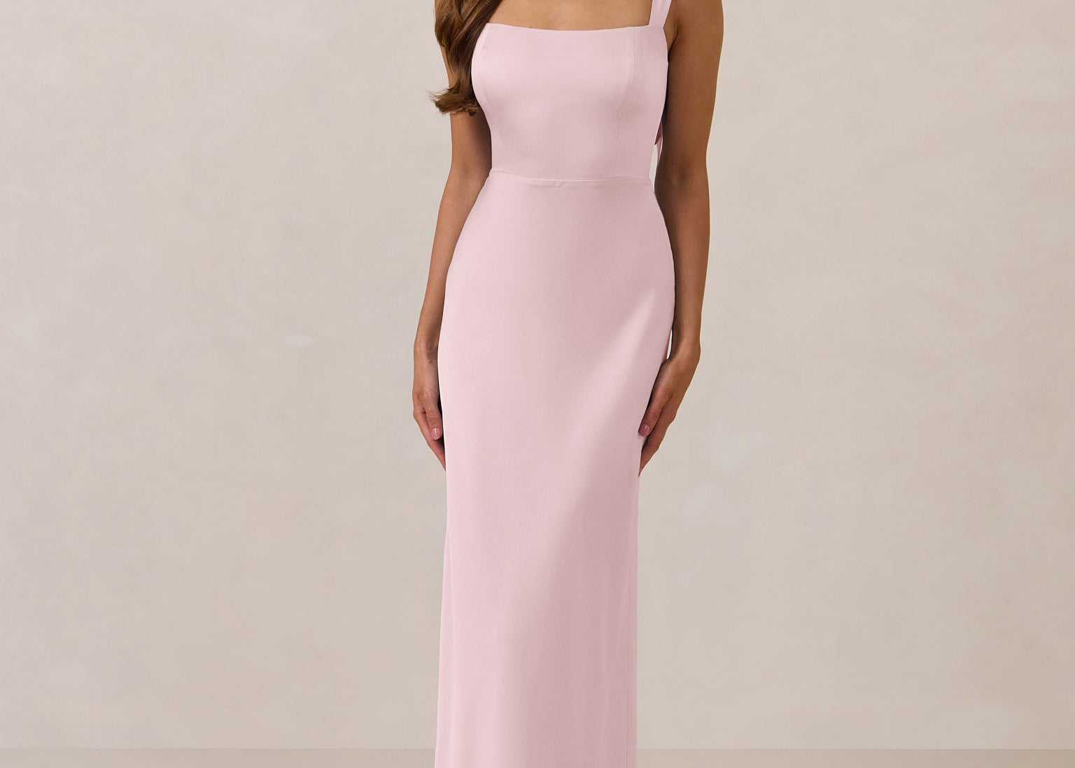 Woman wearing a long light pink dress against a plain background