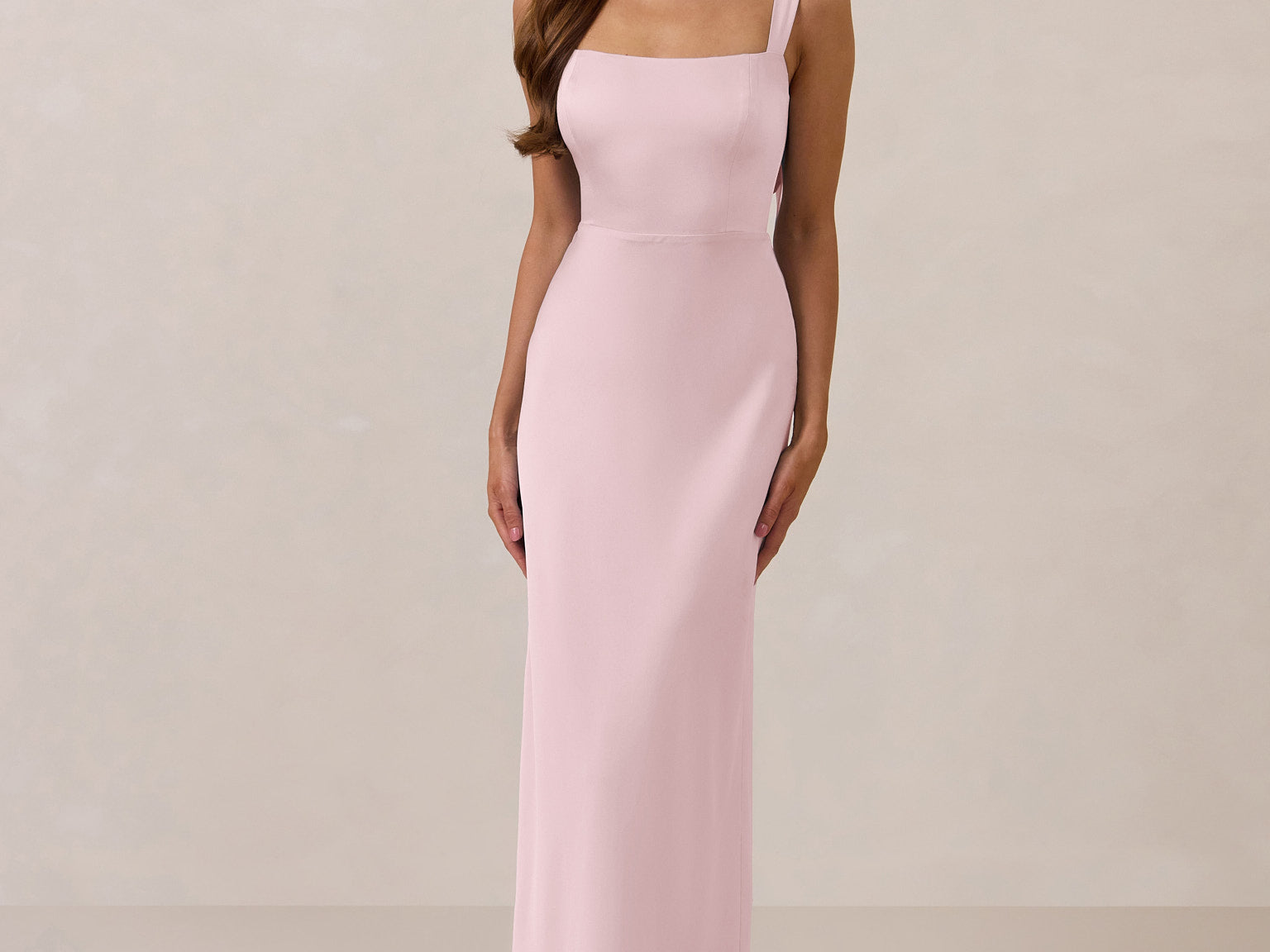 Woman wearing a long light pink dress against a plain background