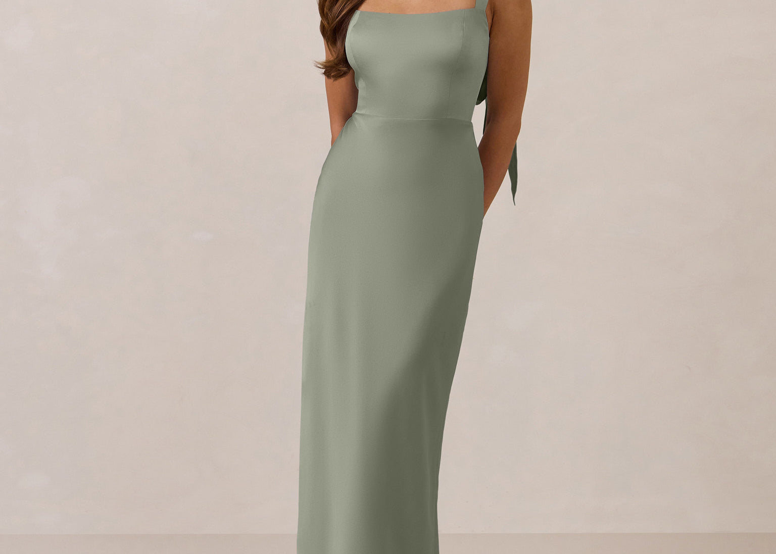 Woman wearing a long true sage dress against a plain background