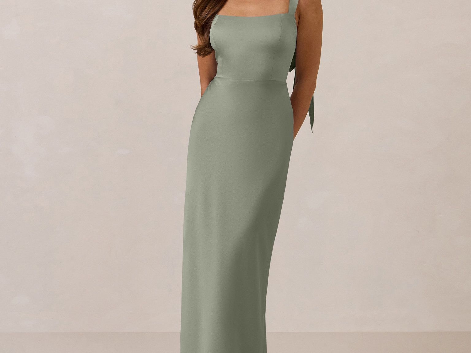 Woman wearing a long true sage dress against a plain background