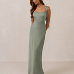 Woman wearing a long true sage dress against a plain background