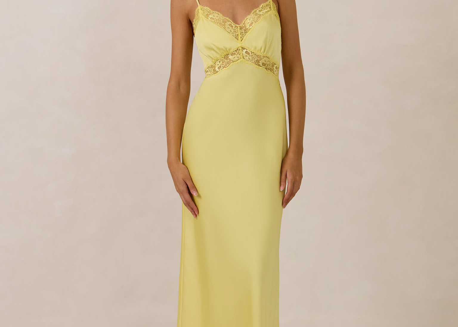 Woman wearing a yellow evening gown with lace detailing on a beige background