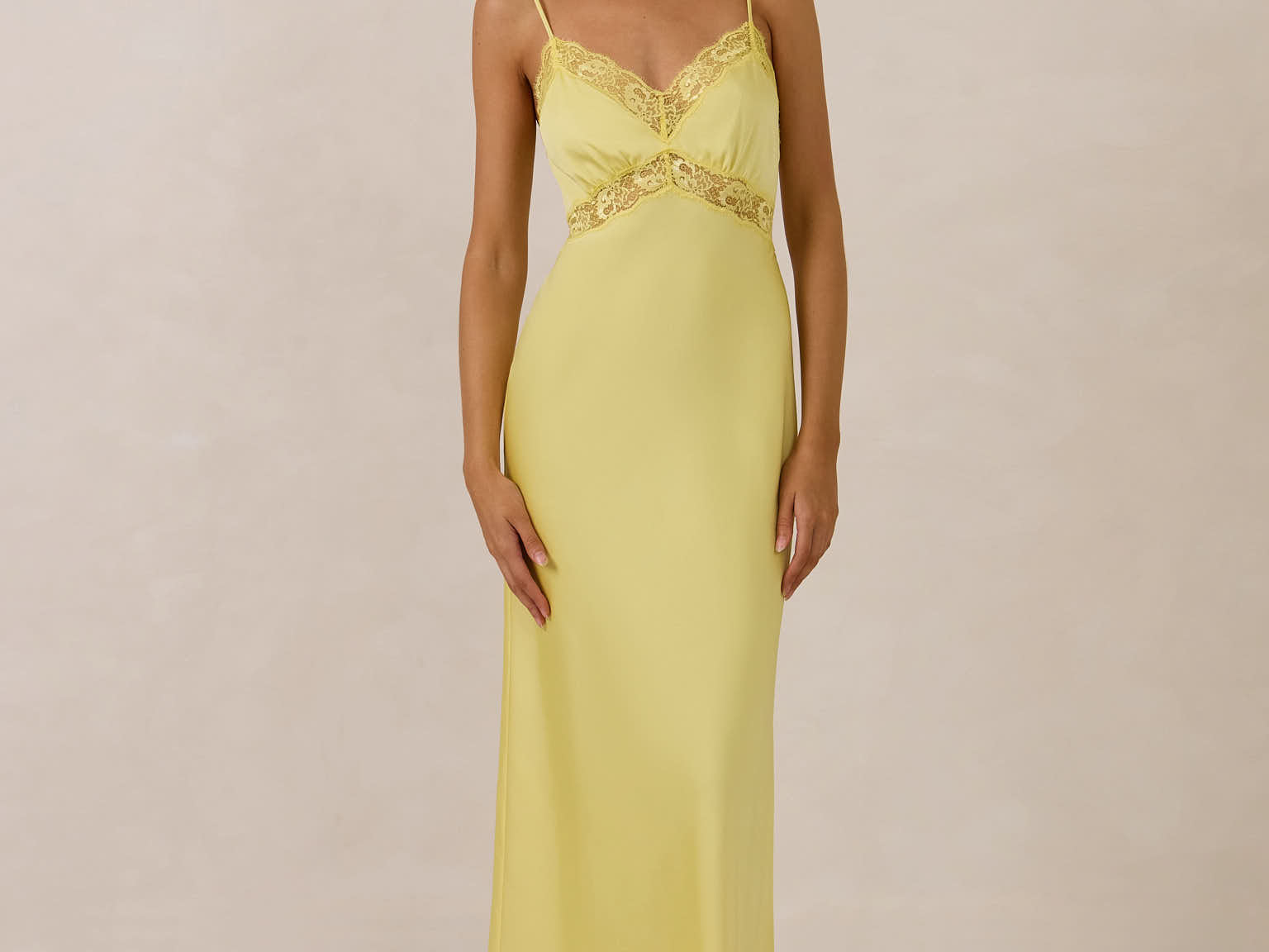 Woman wearing a yellow evening gown with lace detailing on a beige background
