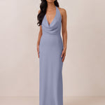 Woman wearing a long, halter style light blue dress against a plain background