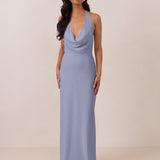 Woman wearing a long, halter style light blue dress against a plain background