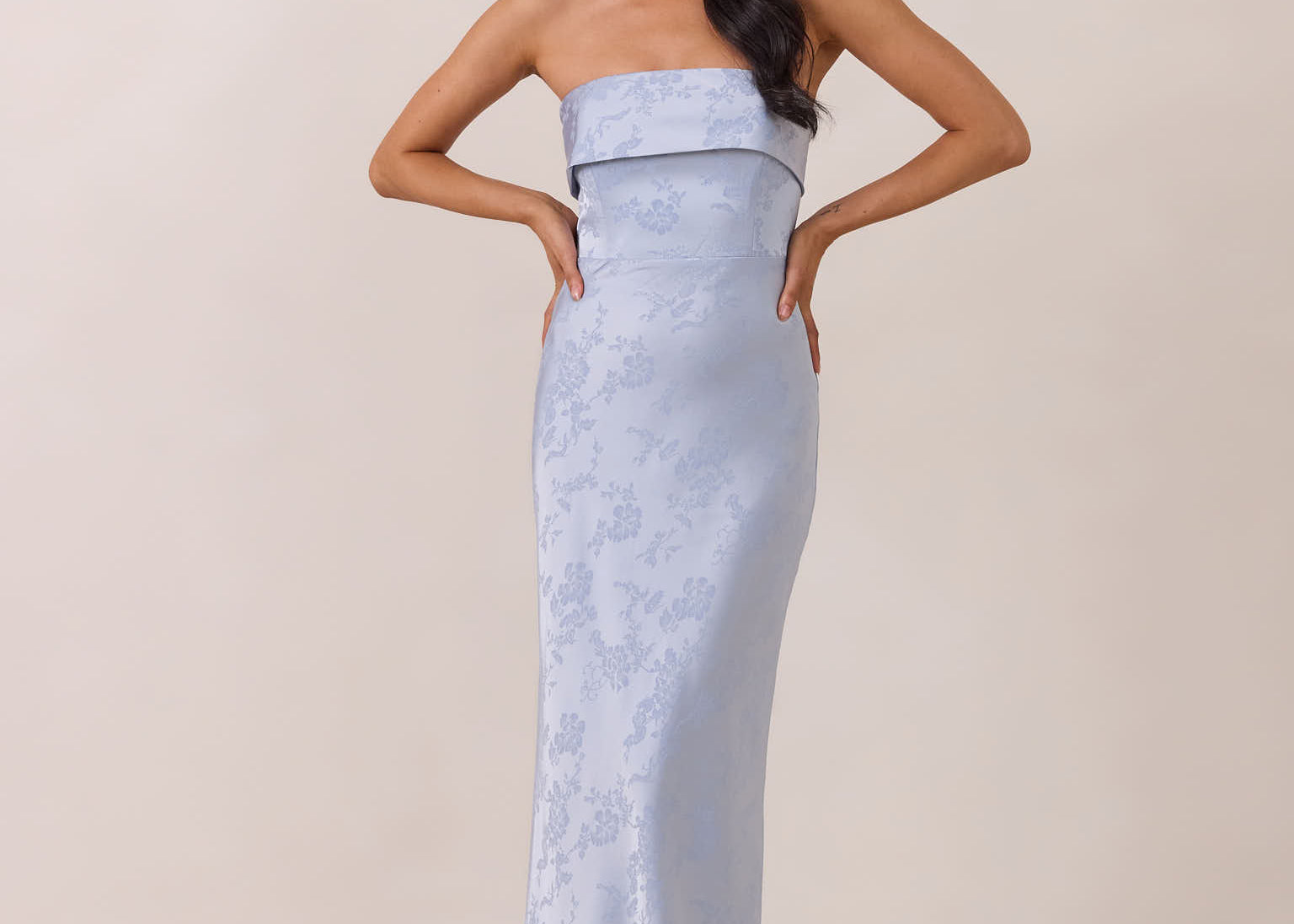 Woman wearing a strapless light blue gown against a beige background