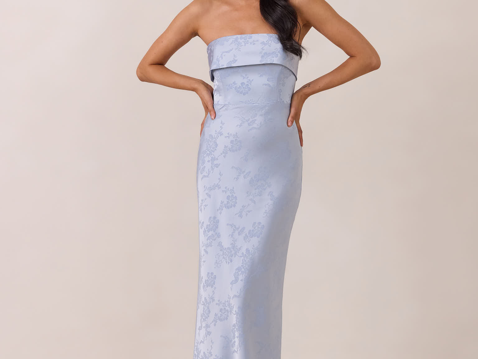 Woman wearing a strapless light blue gown against a beige background