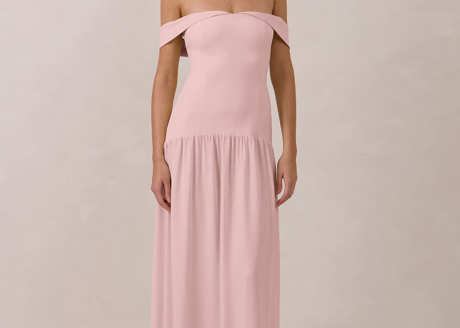 Woman wearing a pink off-shoulder chiffon gown against a plain background