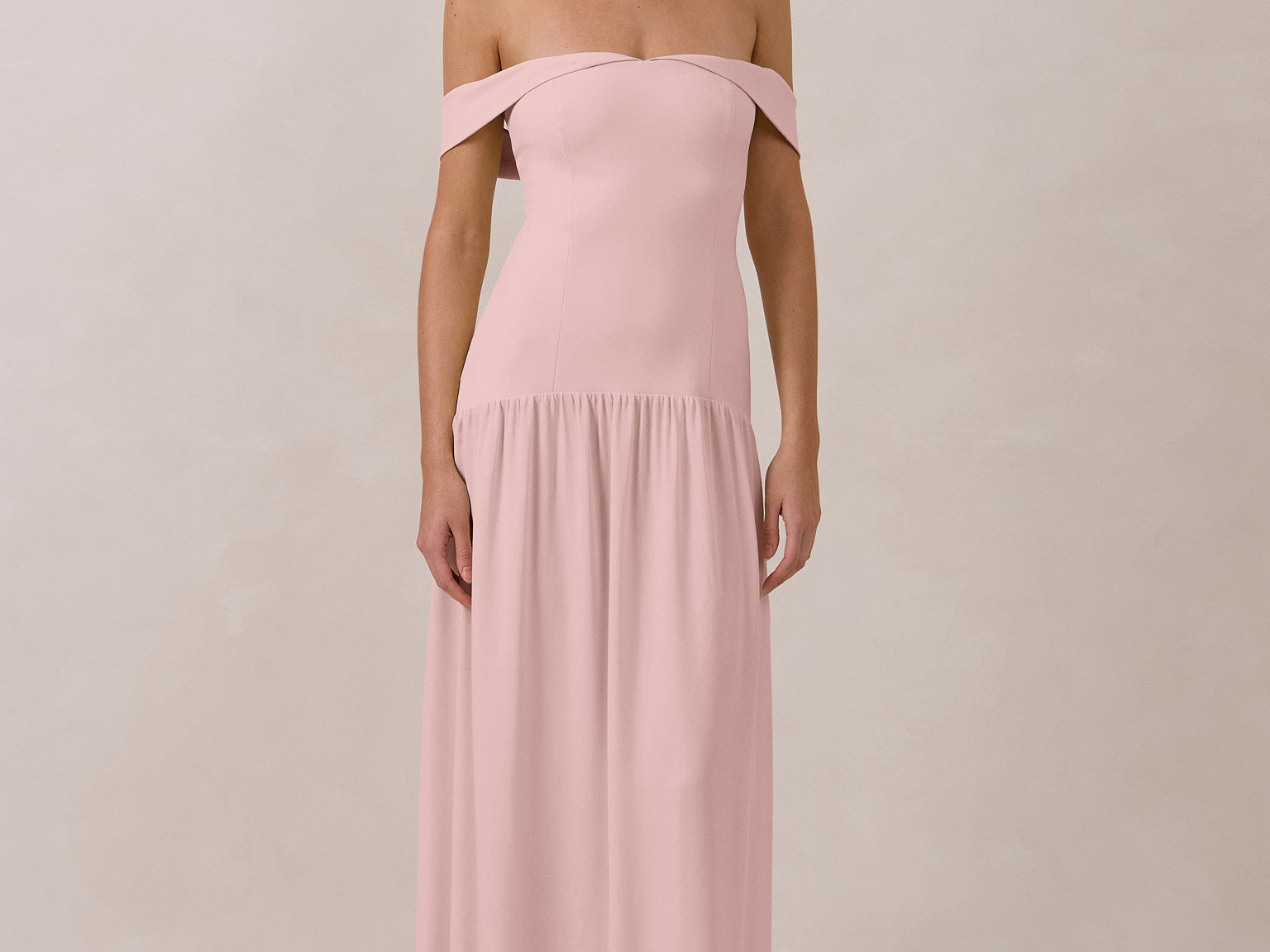 Woman wearing a pink off-shoulder chiffon gown against a plain background