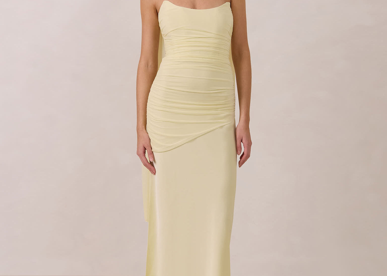 Woman wearing a light yellow strapless gown and neck scarf standing against a plain background