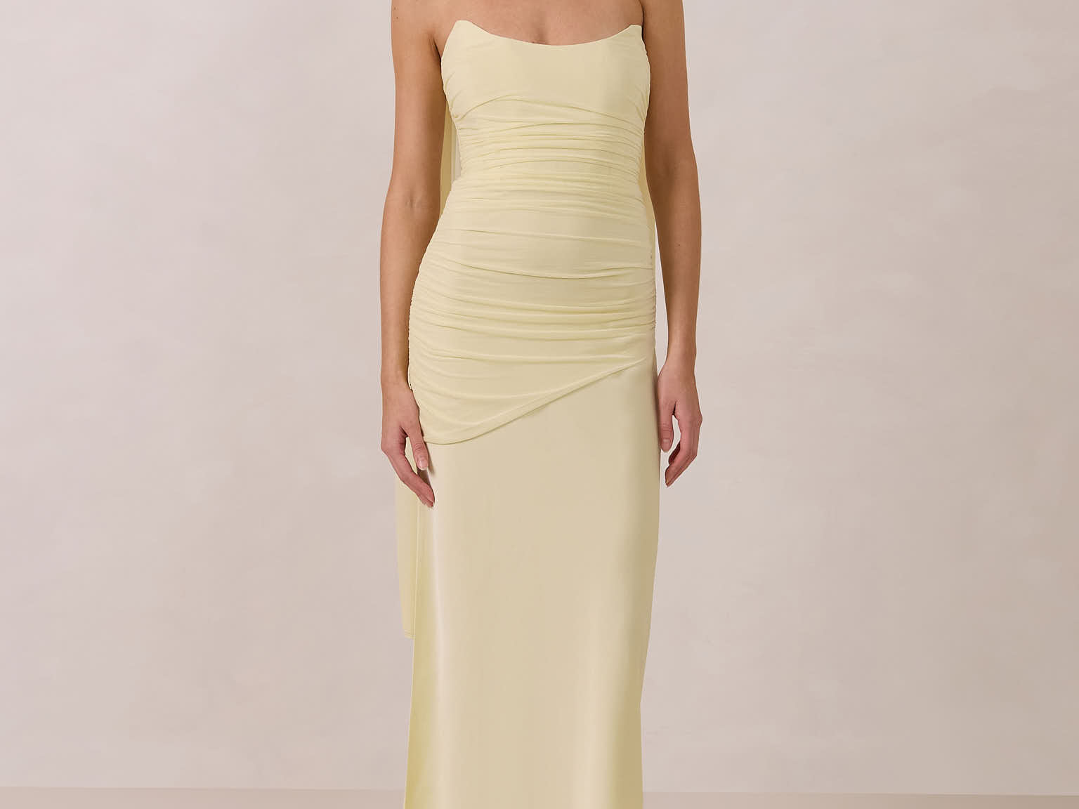Woman wearing a light yellow strapless gown and neck scarf standing against a plain background