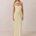 Woman wearing a light yellow strapless gown and neck scarf standing against a plain background