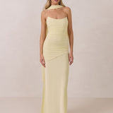 Woman wearing a light yellow strapless gown and neck scarf standing against a plain background