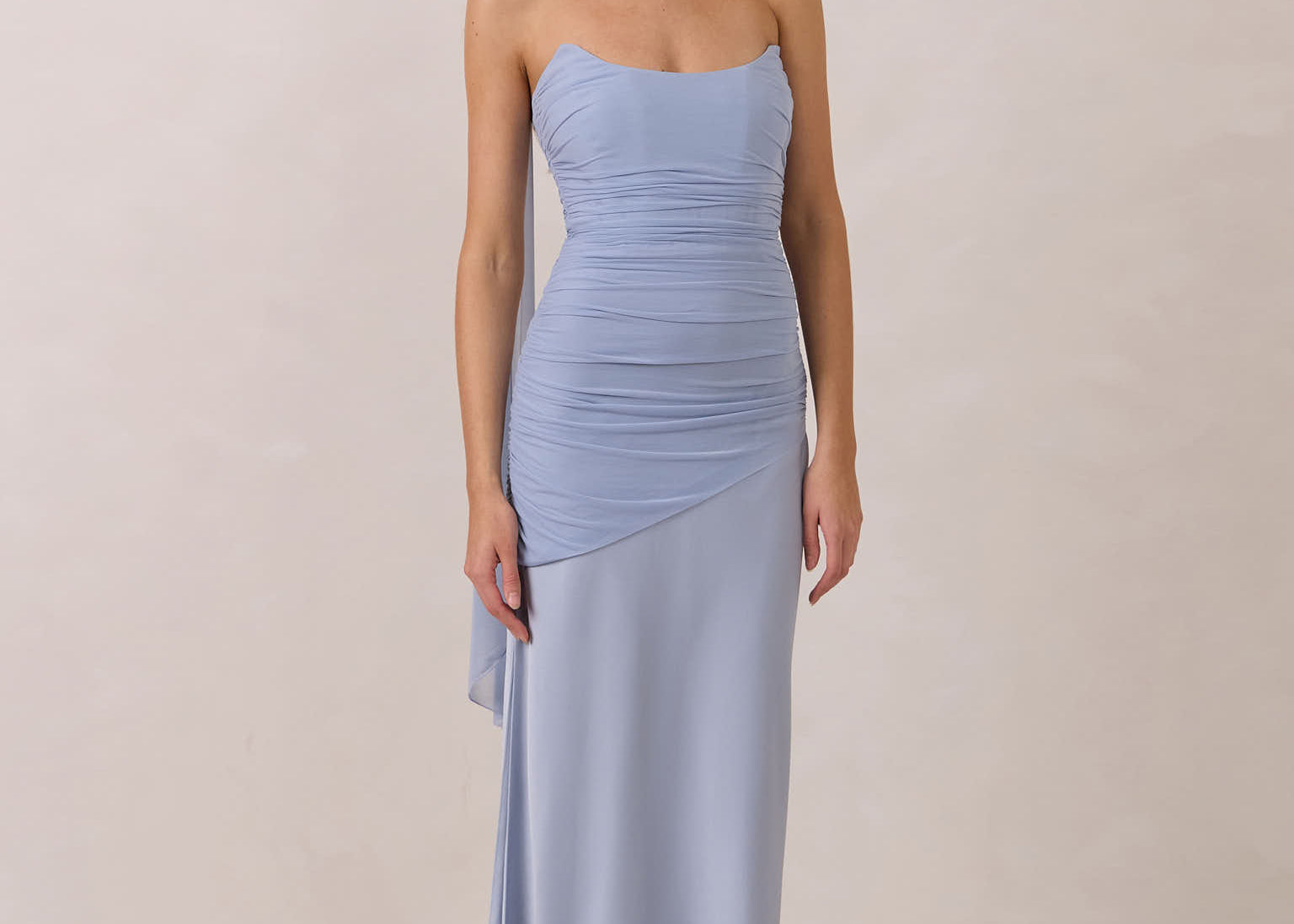 Woman wearing a light blue strapless gown with ruching against a plain background