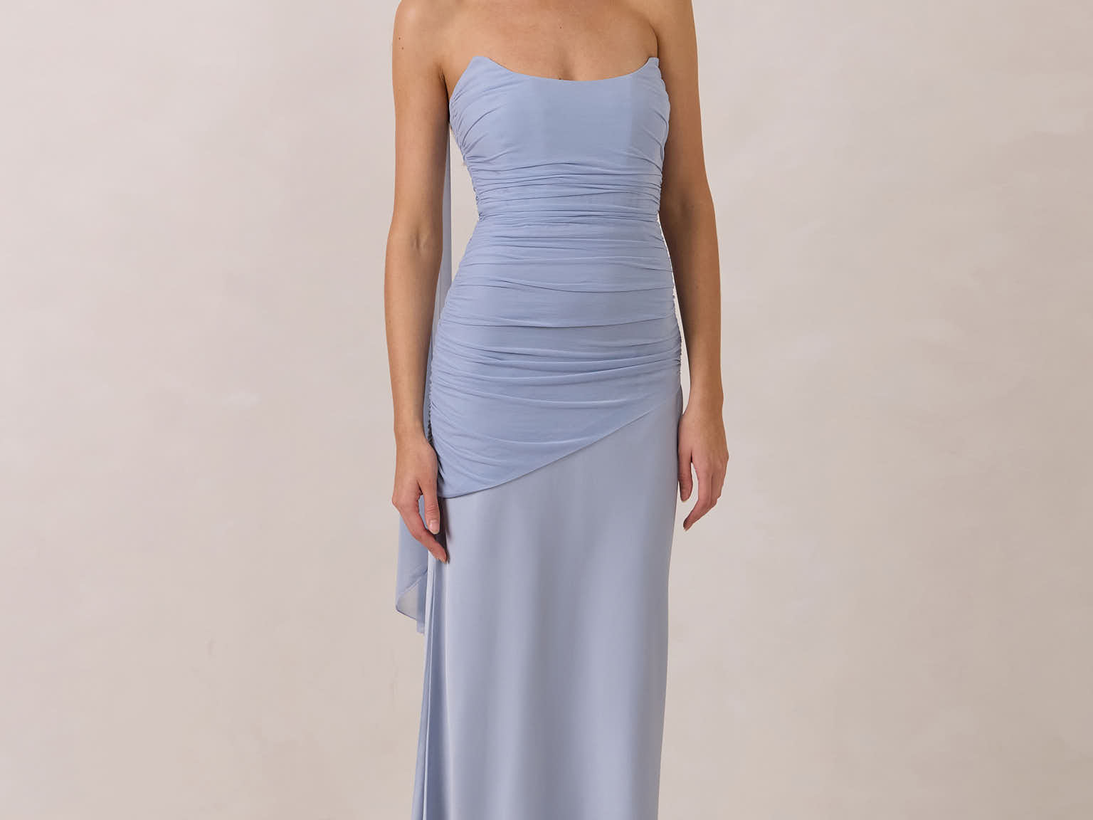 Woman wearing a light blue strapless gown with ruching against a plain background