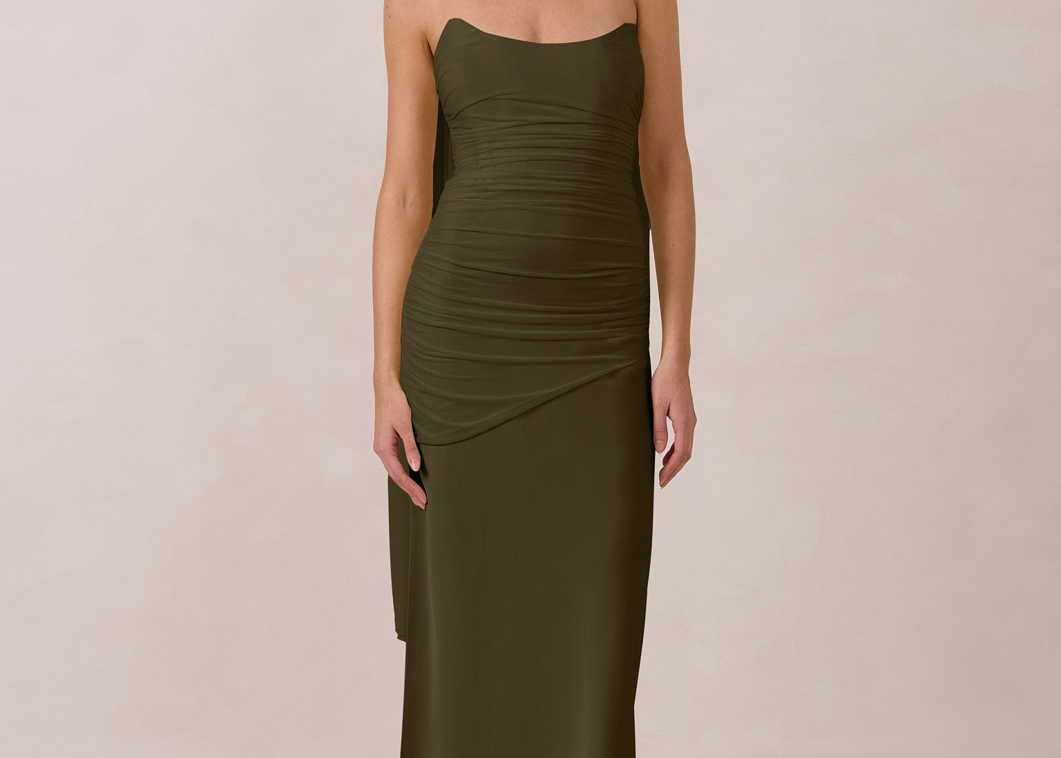 Woman wearing an olive green halter neck dress with ruching throughout the bodice against a plain background