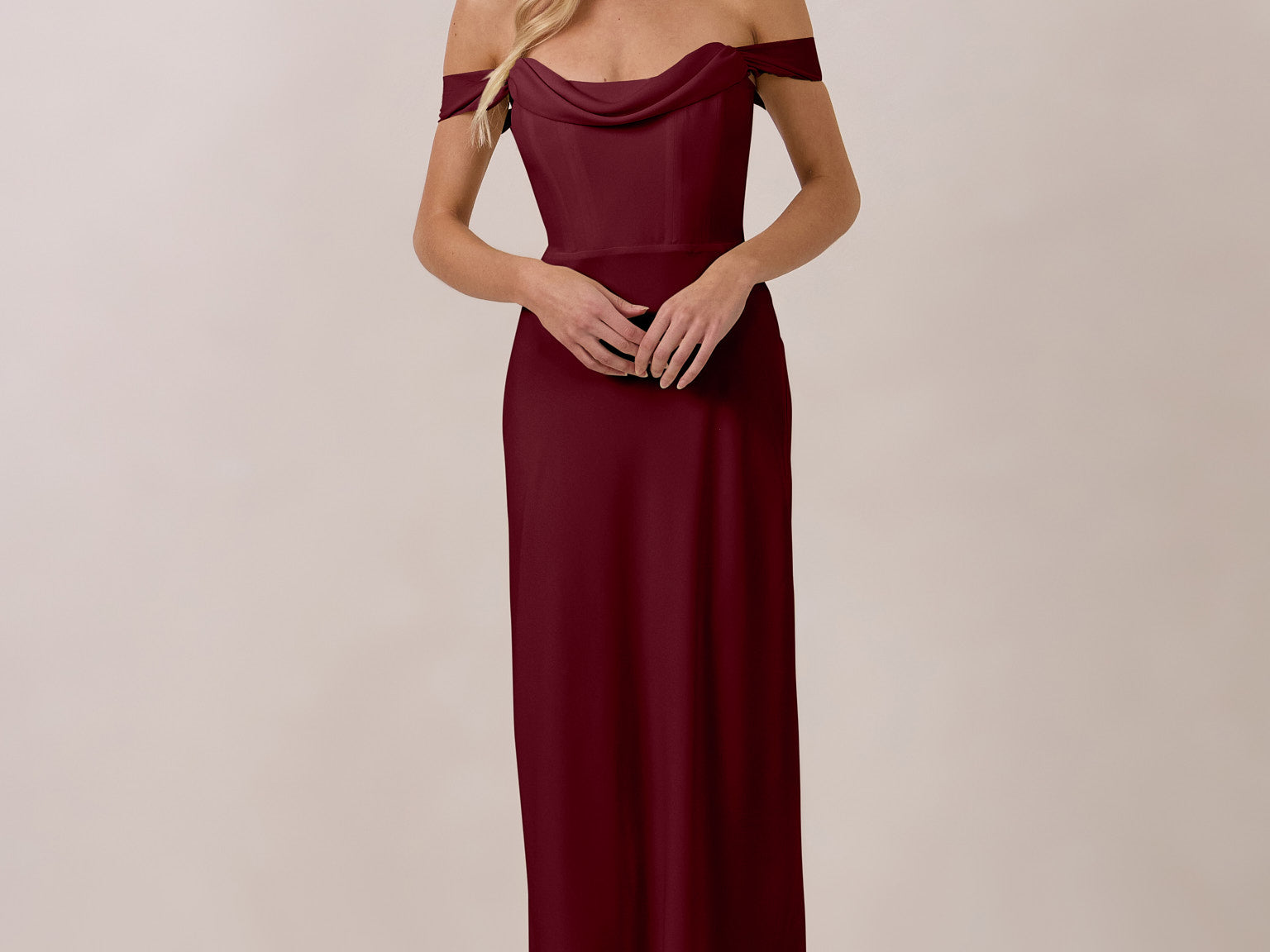 Woman wearing a burgundy off-shoulder dress against a plain background