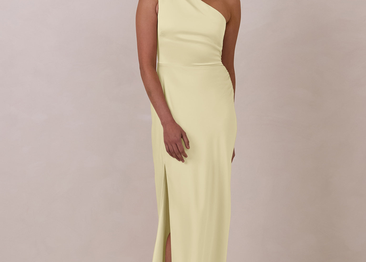 Woman wearing a light yellow one-shoulder gown against a plain background