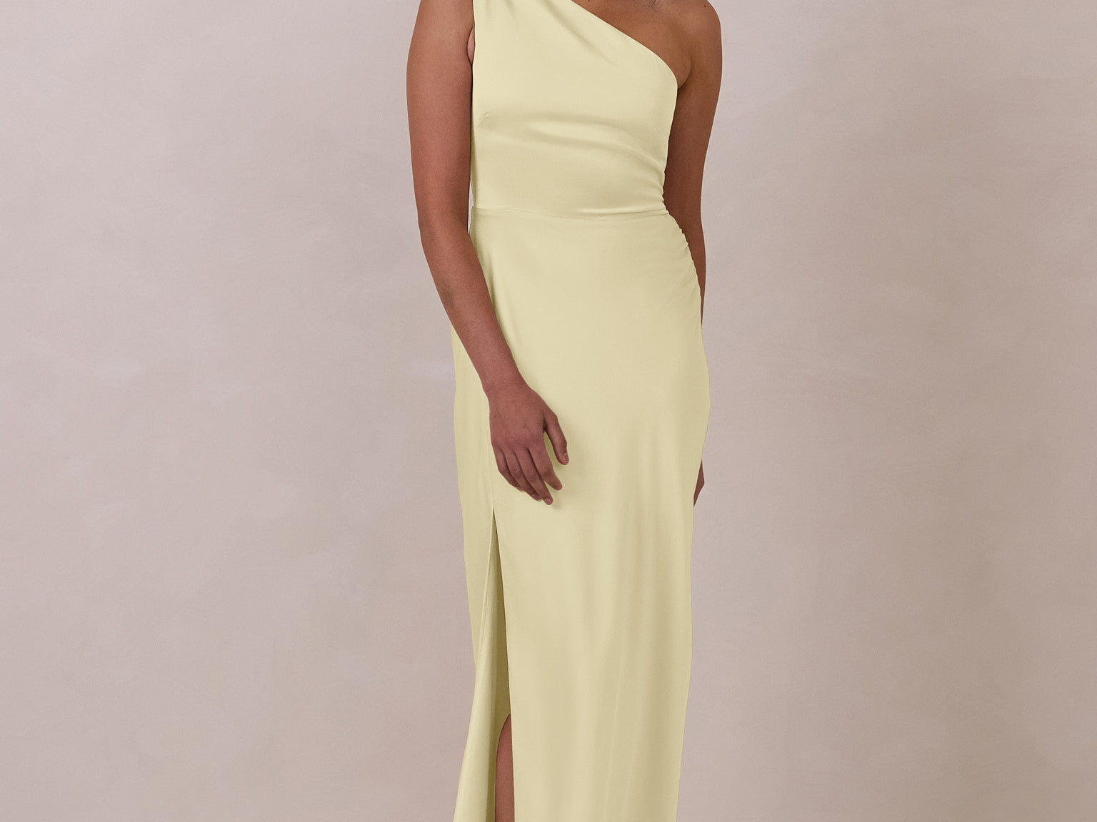 Woman wearing a light yellow one-shoulder gown against a plain background