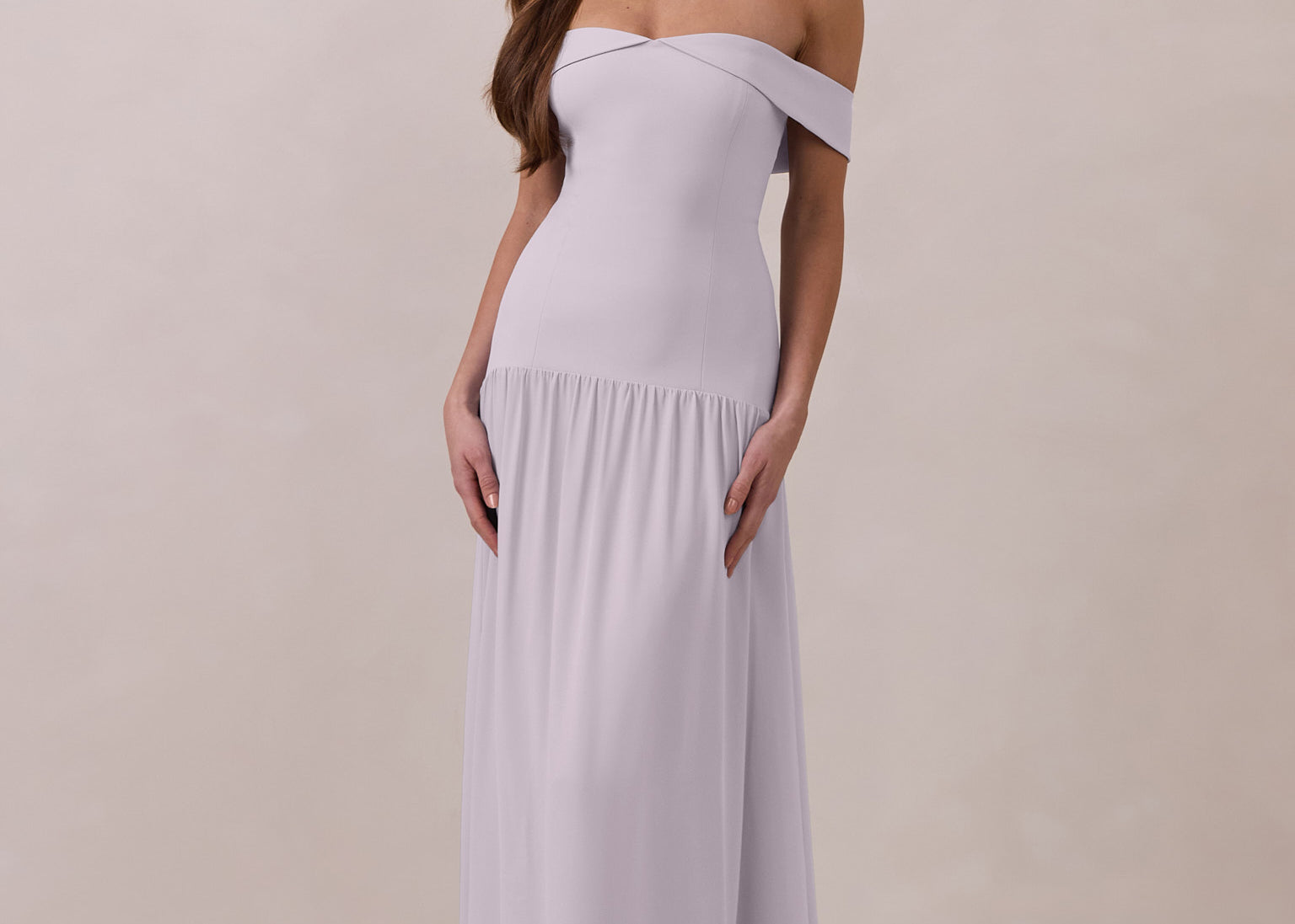 Woman wearing a light purple off-shoulder chiffon gown against a plain background