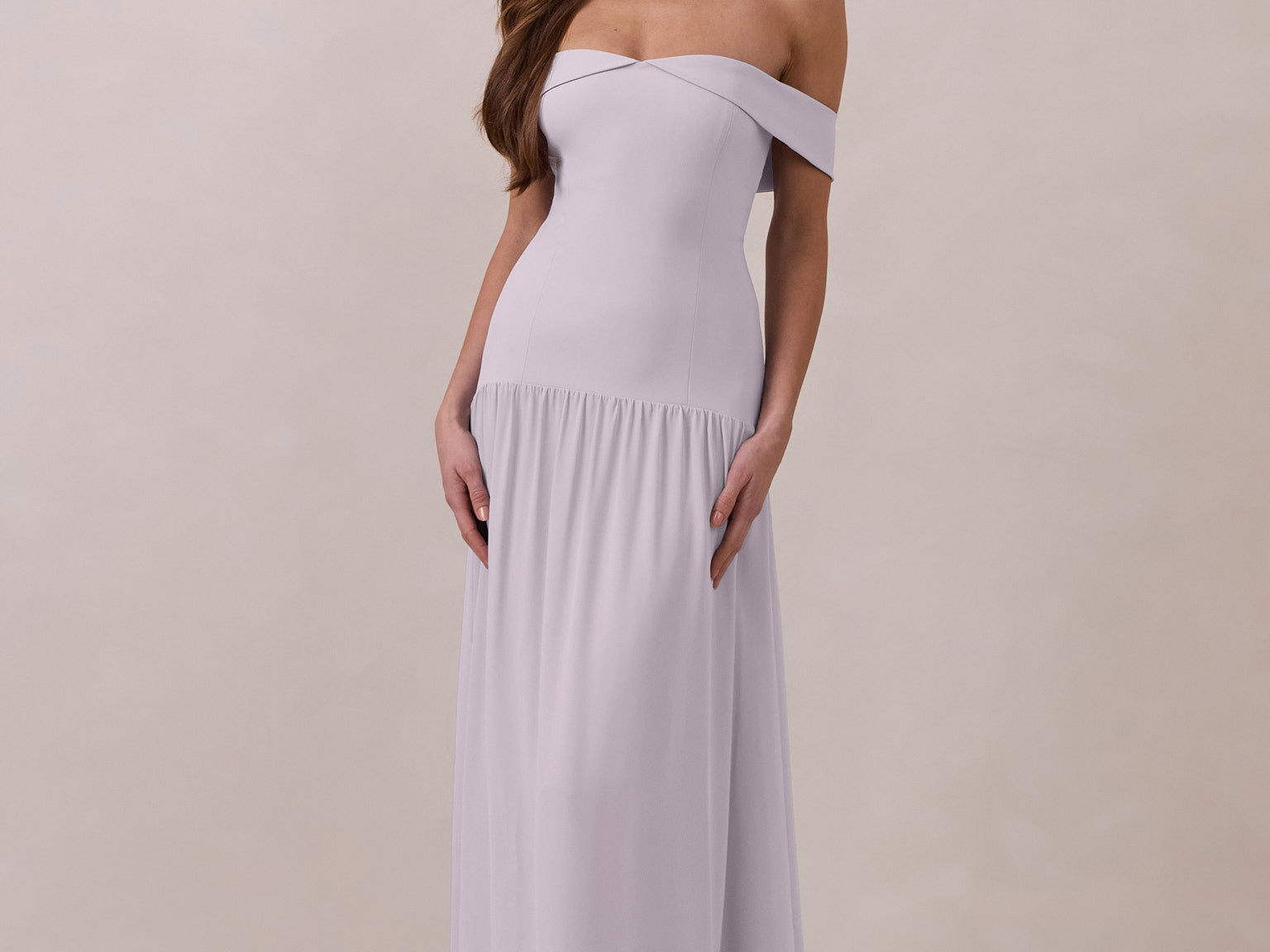 Woman wearing a light purple off-shoulder chiffon gown against a plain background