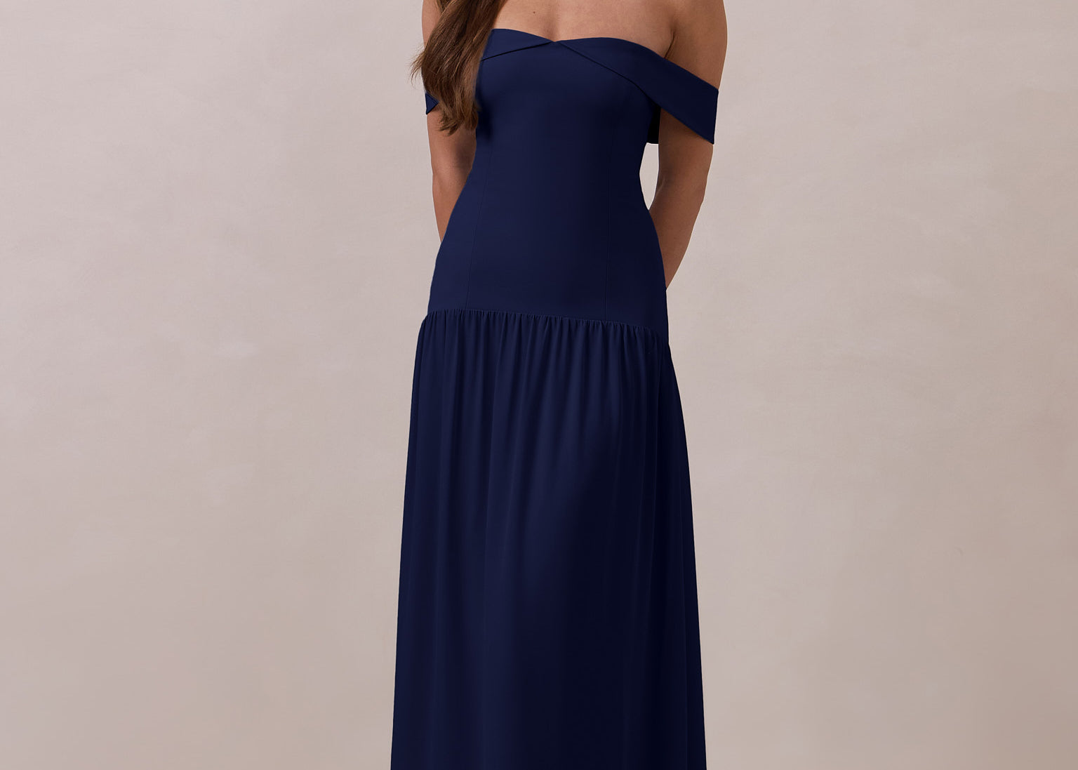 Woman wearing a navy off-shoulder gown with a drop waist standing against a beige background