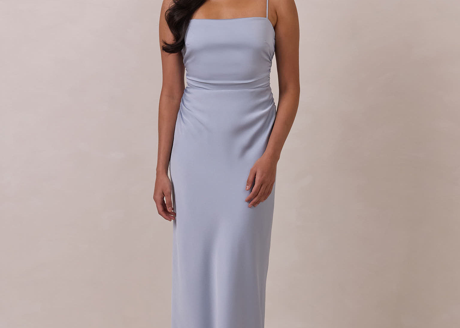 Woman wearing a light blue dress with thin straps standing against a plain background