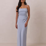 Woman wearing a light blue dress with thin straps standing against a plain background