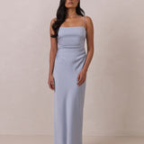 Woman wearing a light blue dress with thin straps standing against a plain background