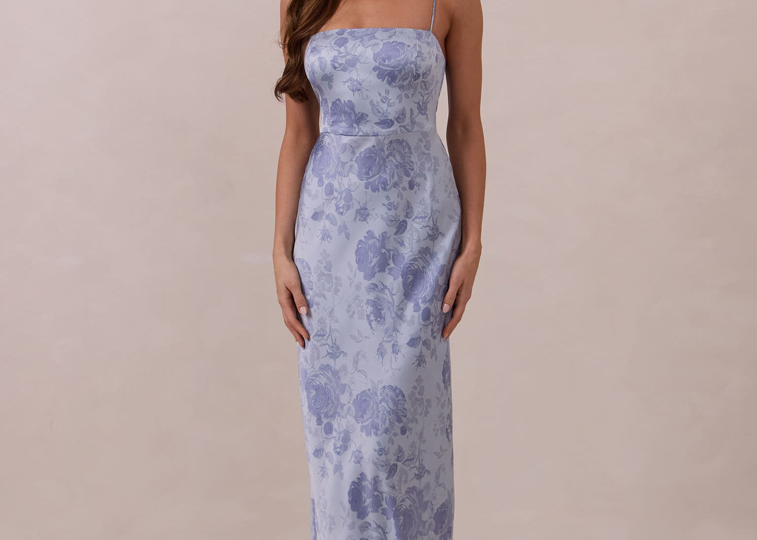 Woman wearing a thin strap floral dress against a plain background