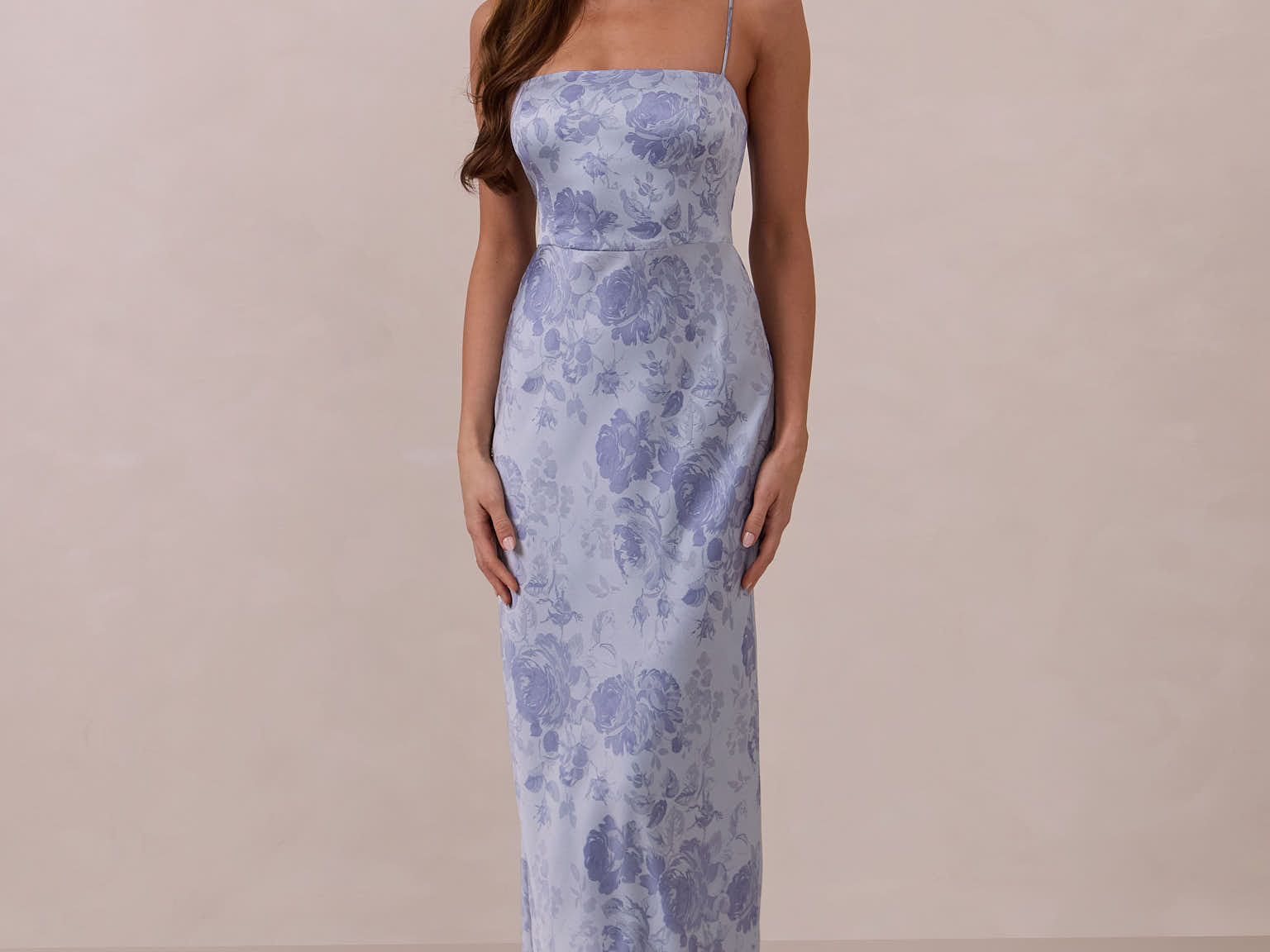 Woman wearing a thin strap floral dress against a plain background