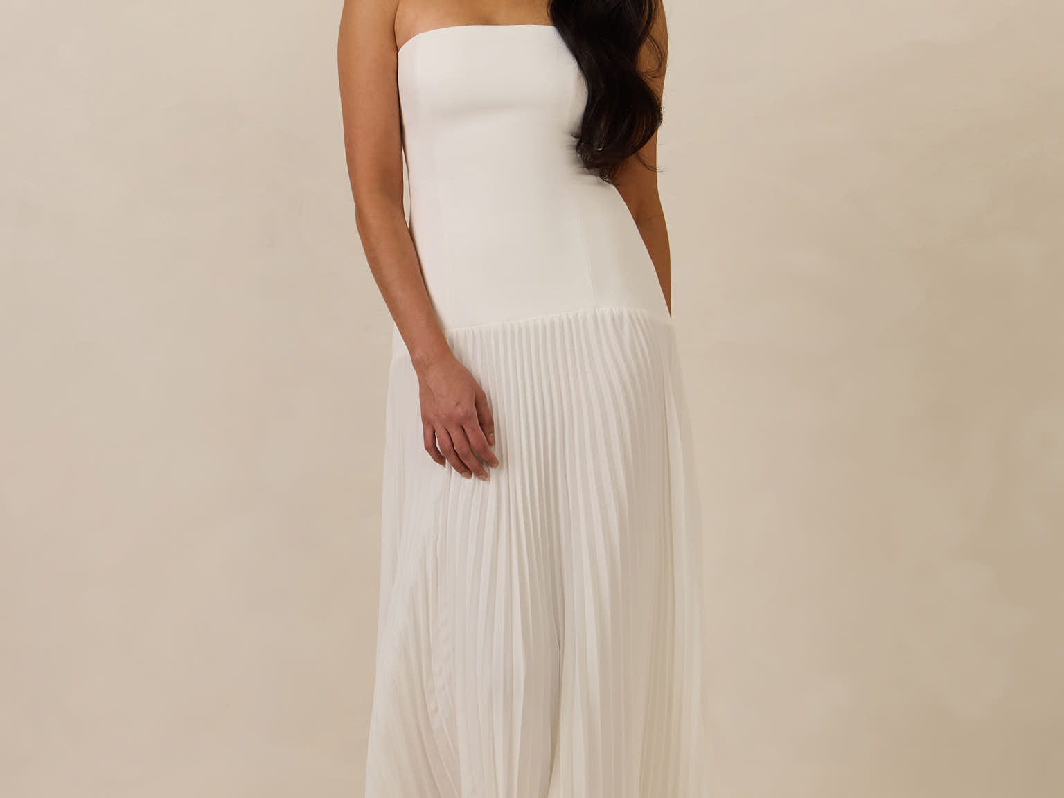 Woman wearing a white strapless gown against a beige background