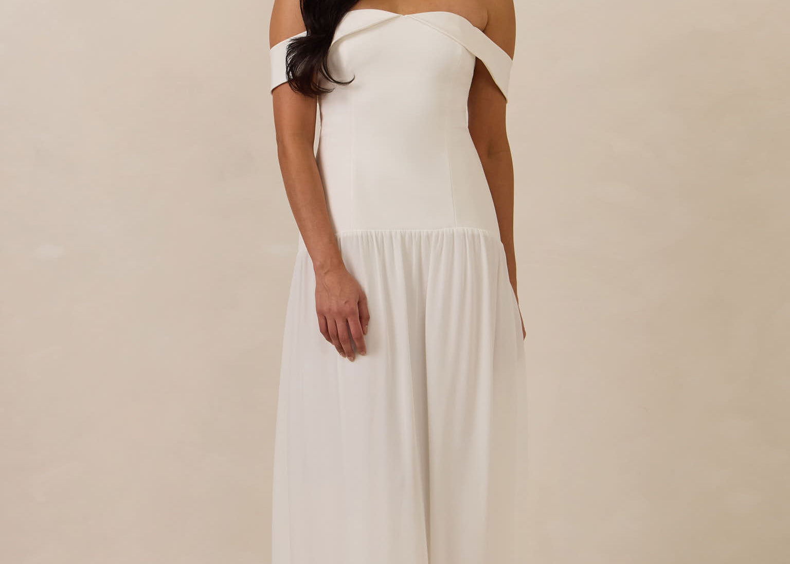 Woman wearing a white off-shoulder dress against a plain background