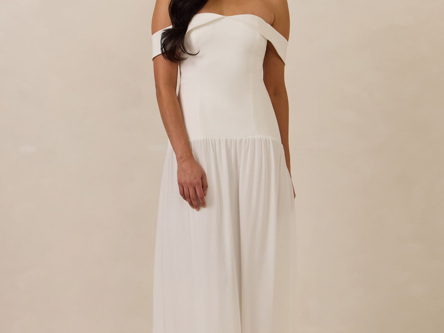 Woman wearing a white off-shoulder dress against a plain background