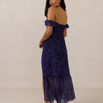 Woman wearing a dark purple floral off the shoulder dress on a beige background