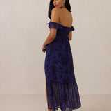 Woman wearing a dark purple floral off the shoulder dress on a beige background