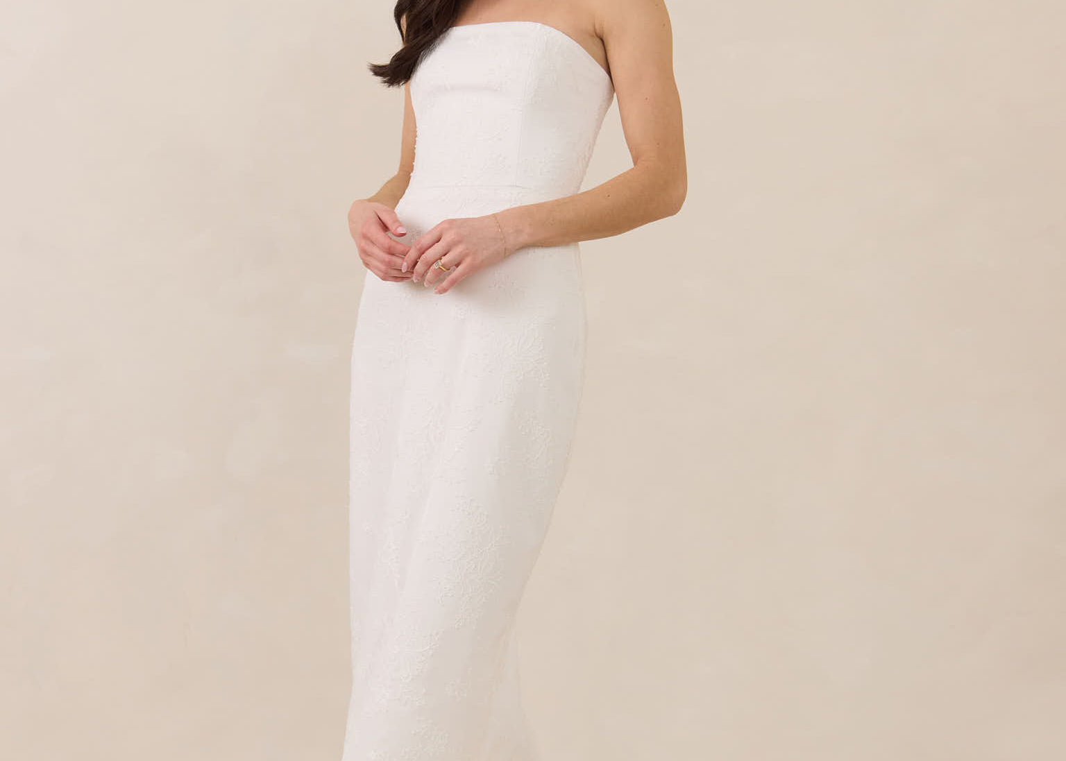 Woman wearing a strapless lace maxi dress on a plain background