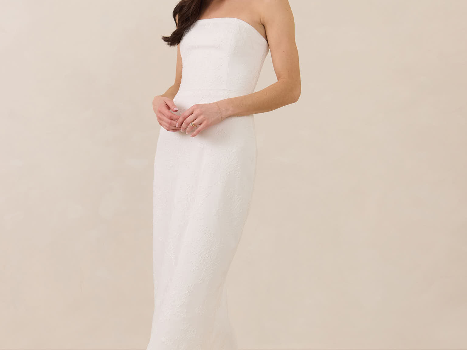 Woman wearing a strapless lace maxi dress on a plain background